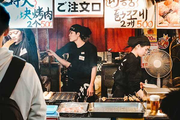 Japanese restaurant workers making hot food in market stall.