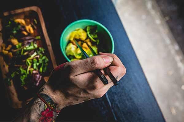Diner using chopstick to eat salad from small bowl.