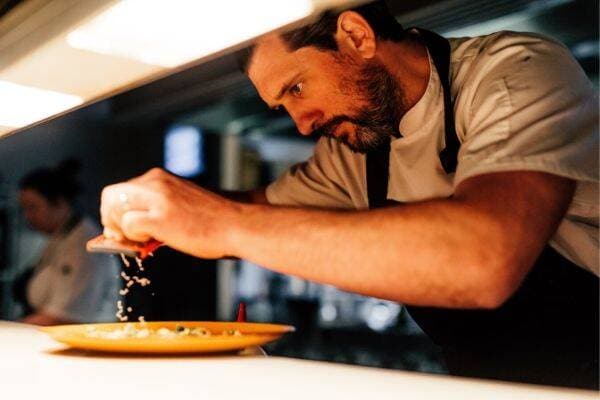 Chef Nick Raitt in kitchen grating cheese over dish before it is served to guests at restaurant.