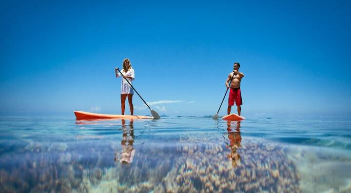 A couple paddleboards through the Mamanucas, gliding over clear water under a bright blue sky.