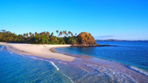 An aerial view of a stunning blue water beach in the Yasawa Islands, showcasing crystal-clear waters gently lapping against white sandy shores.