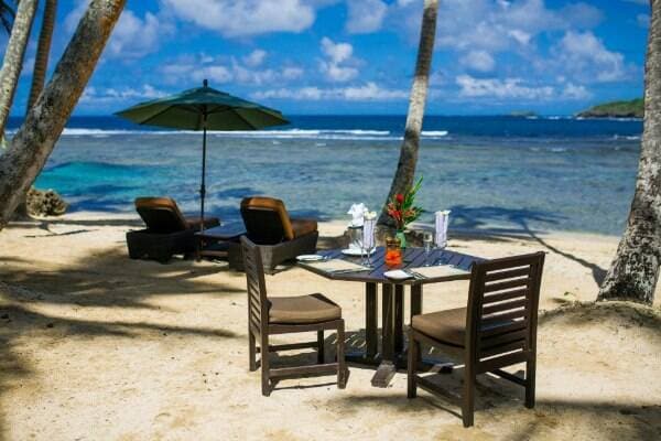 A beautifully arranged dining setup on the sandy beach at Namale Resort, positioned right at the shore. The table offers a stunning view of the water and horizon, creating a romantic and tranquil atmosphere for guests.