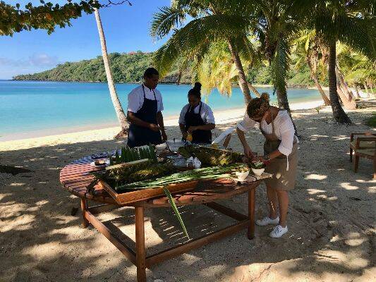Locals at Wakaya Island Resort prepare fresh produce for a meal in traditional style, showcasing vibrant fruits and vegetables. 