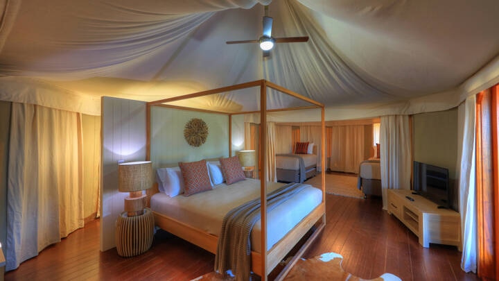 An indoor glamping setup in the Safari tent room at Rivershore, featuring cozy beds, stylish decor, a TV, and a fabric ceiling tent. 